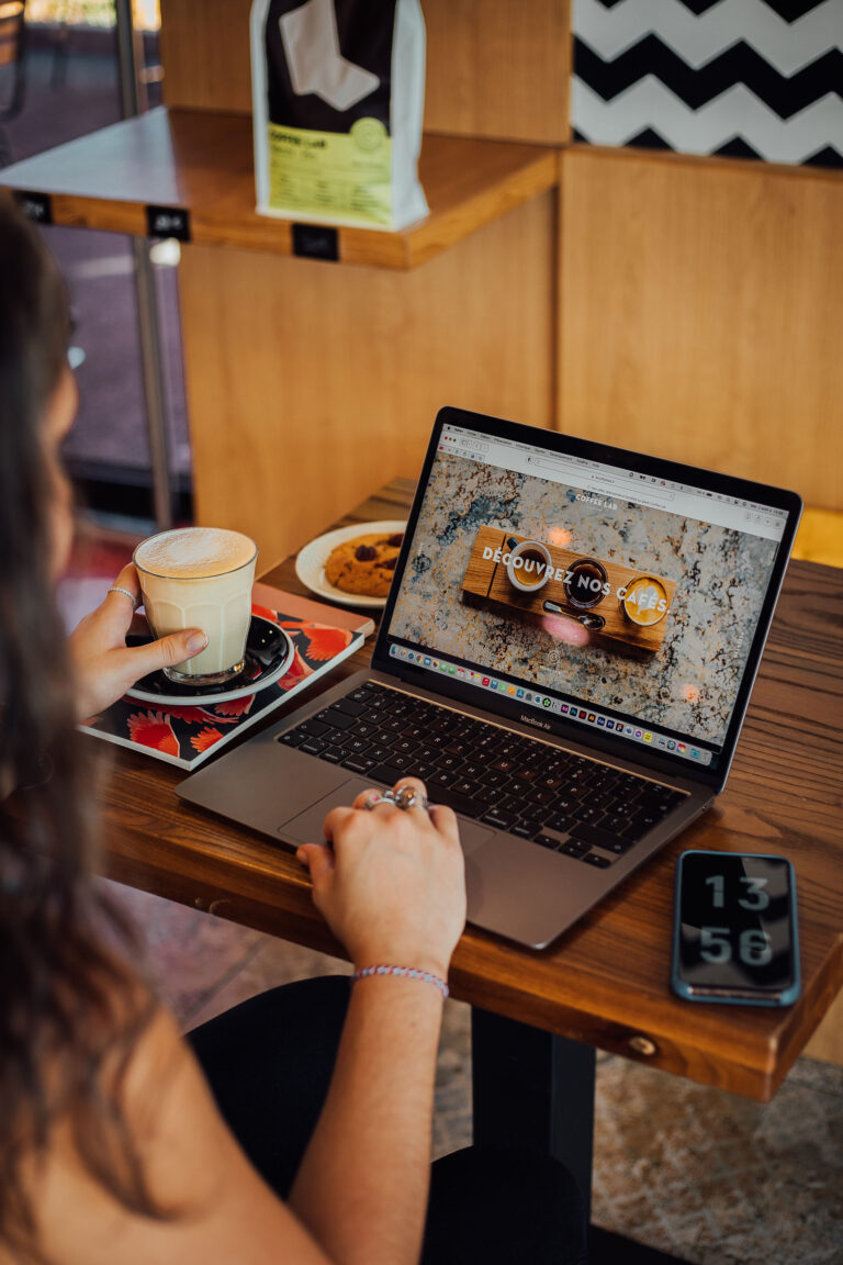 Personne travaillant sur un ordinateur portable dans un café avec une tasse de café à la main, illustrant l’effet du café sur la concentration